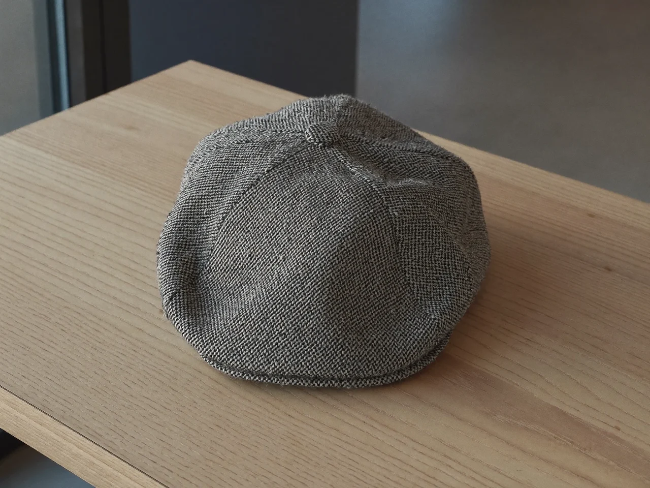 Flat cap i tweed med fiskebensmønster på et lyst træbord