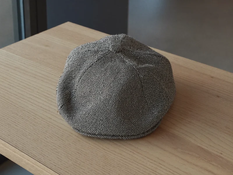Flat cap i tweed med fiskebensmønster på et lyst træbord